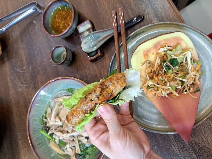 Personne tenant un rouleau de printemps et une garniture au-dessus d'une assiette avec de la salade.