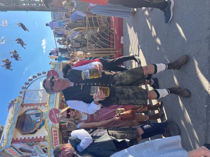 Person holding two beer steins at an outdoor festival.