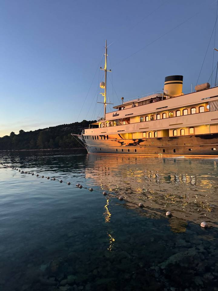 Grand yacht amarré sur une eau calme au coucher du soleil avec un reflet dans l'eau.