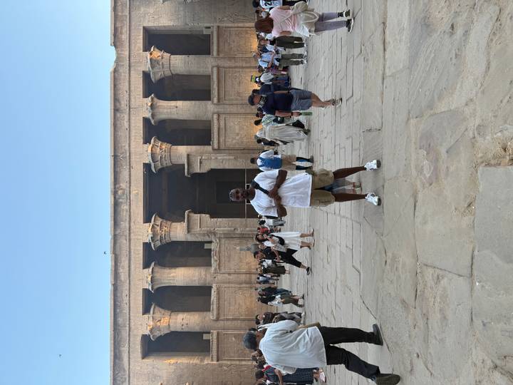 Man standing in front of an ancient Egyptian temple with a group of tourists.