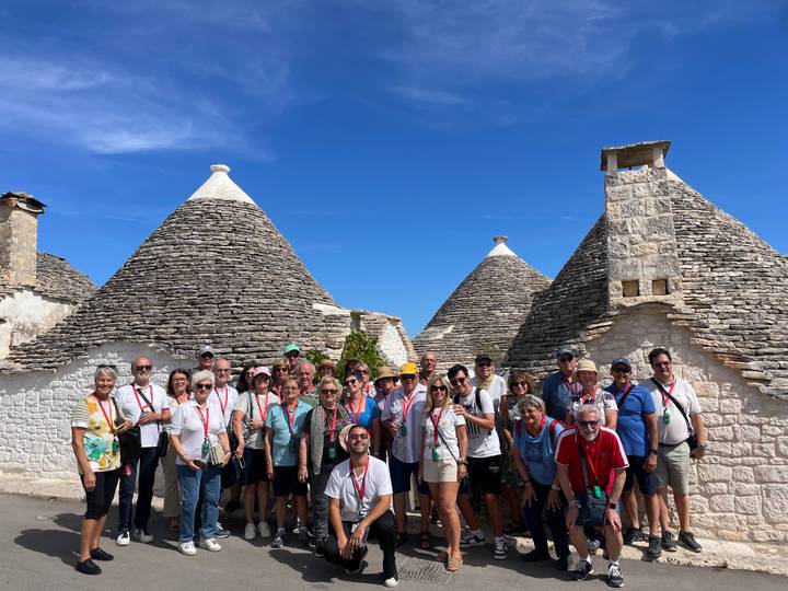 Grand groupe de touristes devant des maisons traditionnelles en pierre aux toits coniques.
