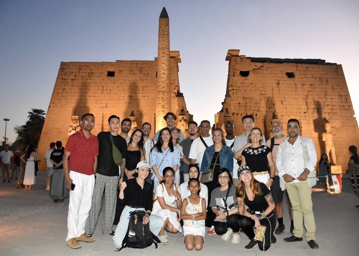 Groupe de personnes posant devant des ruines antiques illuminées