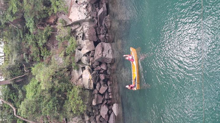 Deux personnes ramant dans un bateau sur une rivière verte et claire le long de rives rocheuses.