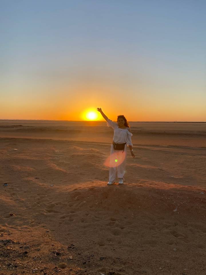 Personne levant la main vers le soleil couchant dans un paysage désertique.