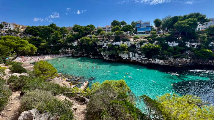 Anse avec une eau claire et des gens qui nagent, entourée de verdure.