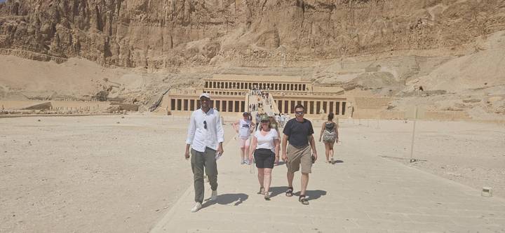 Des touristes marchant vers un ancien temple égyptien sculpté dans une paroi rocheuse.
