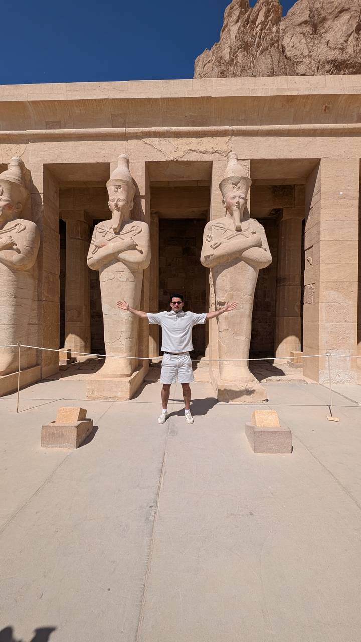 Homme posant avec des statues de temple ancien derrière.