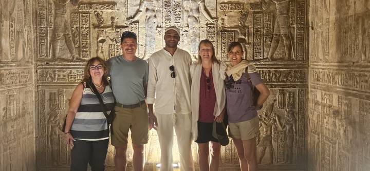 A group of tourists standing inside an Egyptian temple with hieroglyphics.