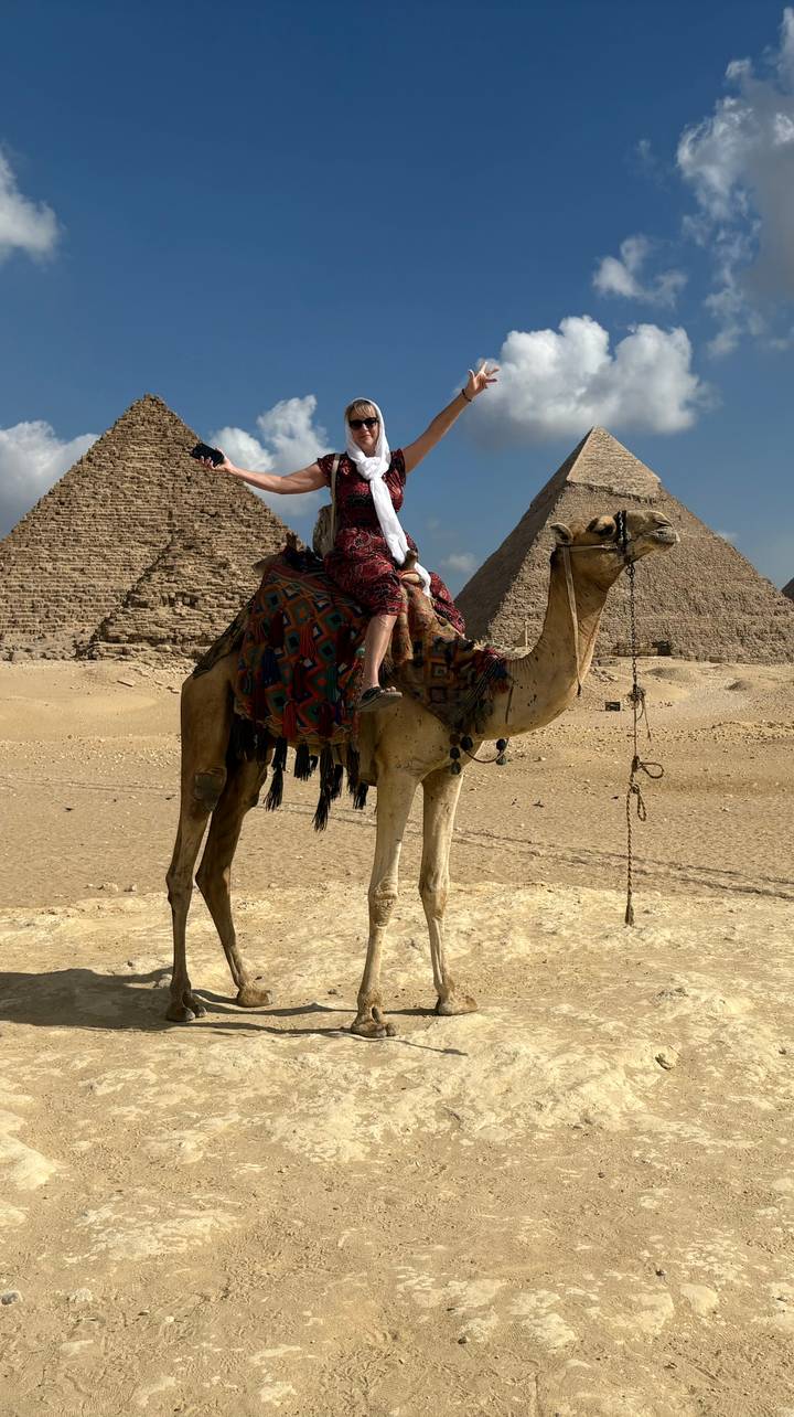 A person on a camel with pyramids in the background.