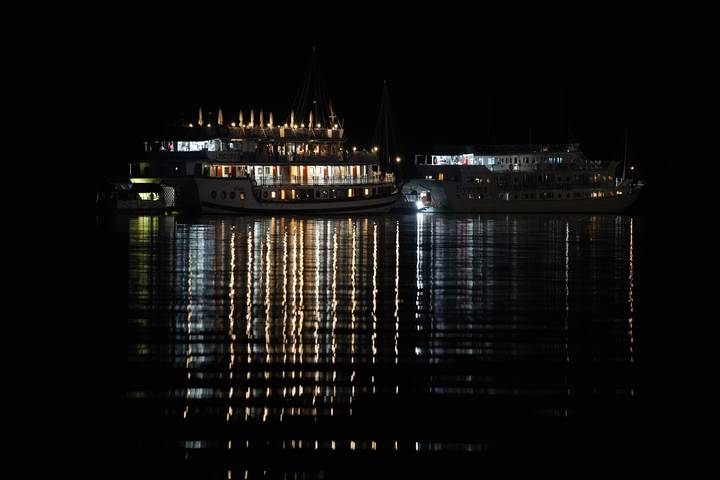 Bateaux illuminés de lumières colorées la nuit, se reflétant sur l'eau.