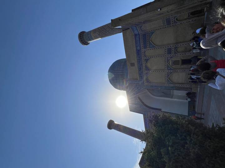 Visiteurs à l'entrée d'une mosquée avec le soleil qui scintille au-dessus.