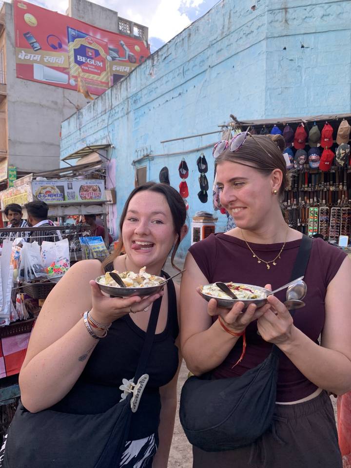 Deux femmes posant avec des assiettes de nourriture à un marché.