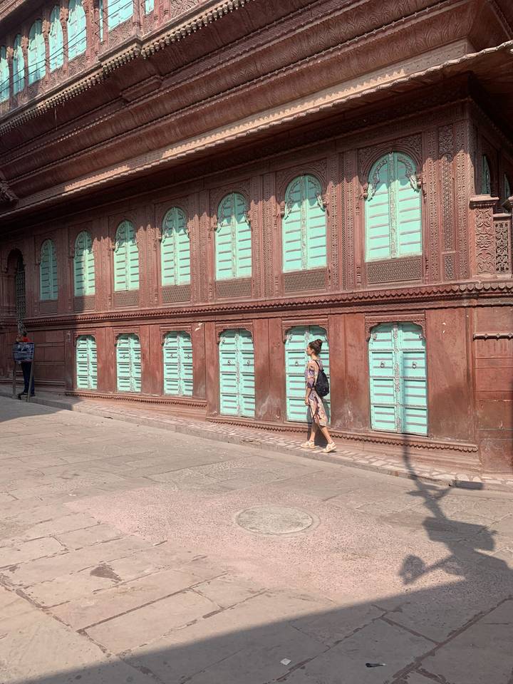 Une femme marchant devant un bâtiment historique avec des volets bleu-vert.