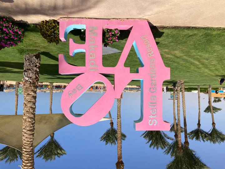 Panneau coloré 'LOVE' aux Jardins de Stella Resort avec palmiers et plage en arrière-plan.