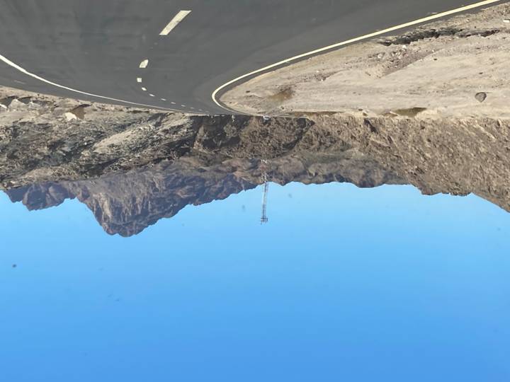 Route désertique menant vers des montagnes rocheuses sous un ciel bleu.