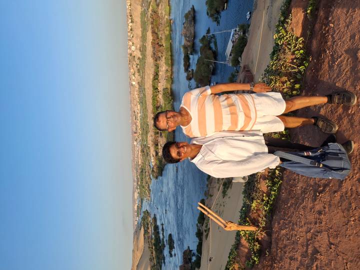 Deux personnes debout sur une colline surplombant une rivière avec une ville en arrière-plan.