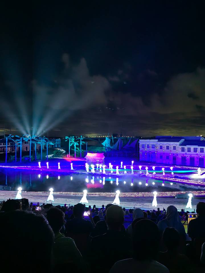 Spectacle nocturne avec des lumières colorées et des figures illuminées près de l'eau.