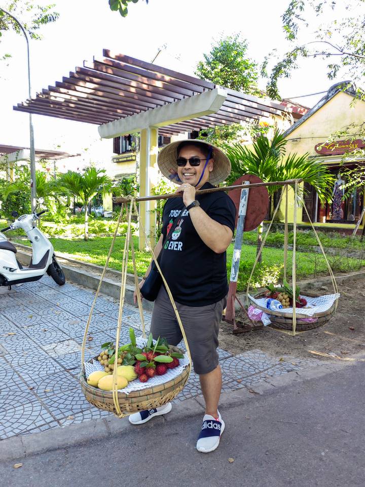 Homme souriant en équilibrant un panier de fruits traditionnel.