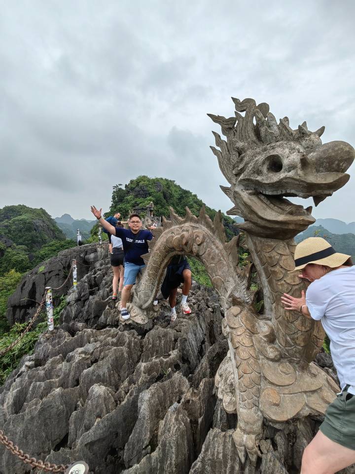Homme grimpant avec une sculpture de dragon et un paysage rocheux.