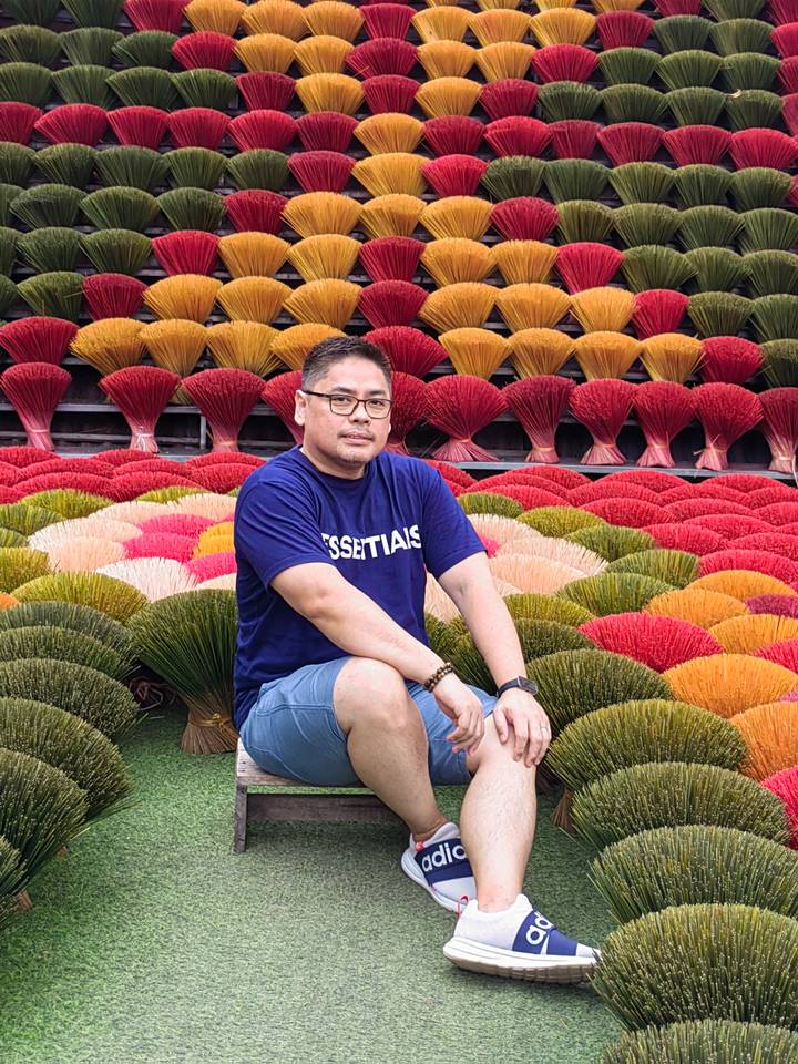 Une personne assise devant des fagots colorés de bâtons d'encens.