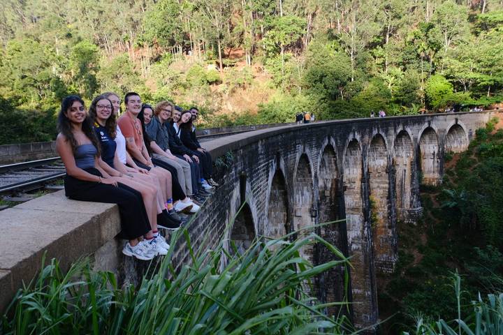 Groupe de personnes assises sur un pont ferroviaire au-dessus d'une vallée verdoyante luxuriante.