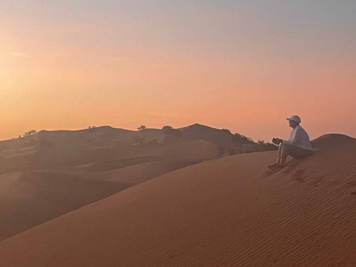 Individu assis sur une dune de sable pendant le coucher du soleil.