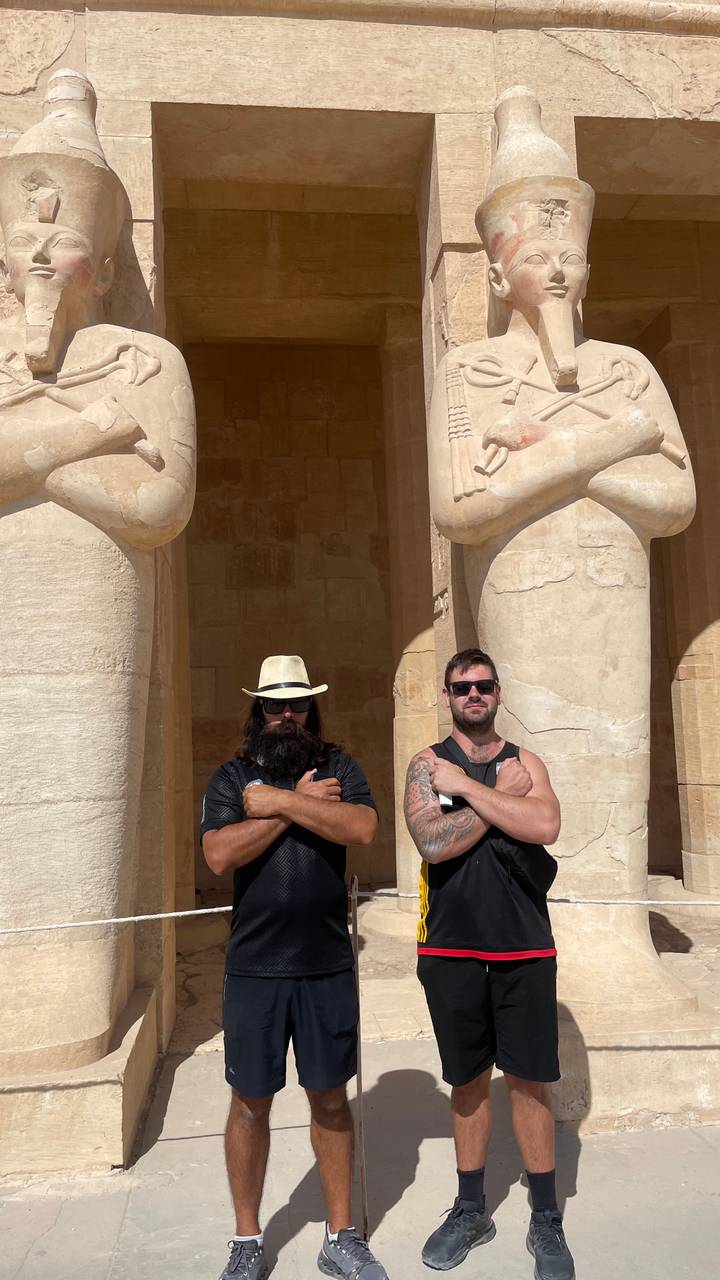 Deux hommes posant devant des colonnes antiques avec les bras croisés.