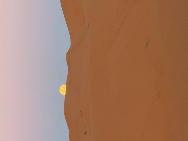 Pleine lune se levant au-dessus des dunes de sable dans un paysage désertique.
