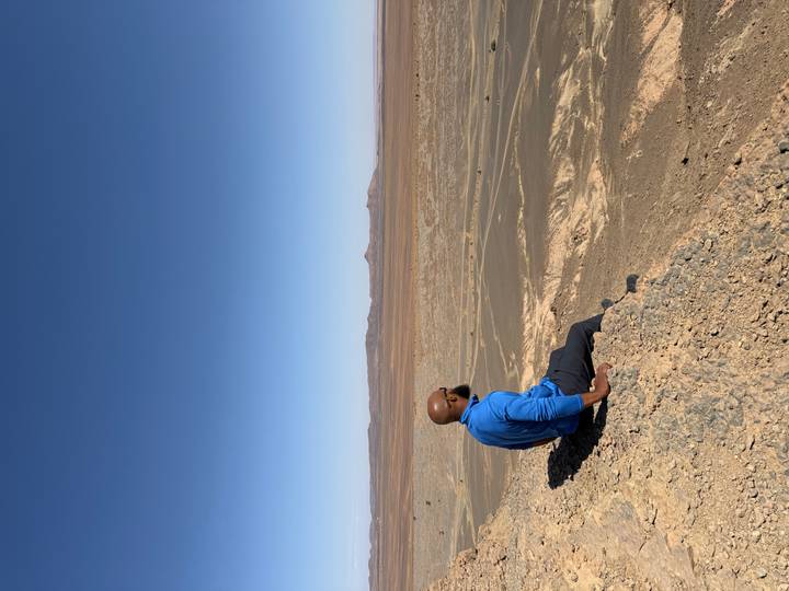 Personne assise regardant un paysage désertique avec des montagnes au loin.