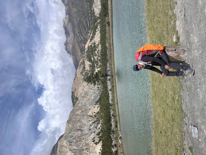 Person resting on a log by a serene lake with mountains in the background.