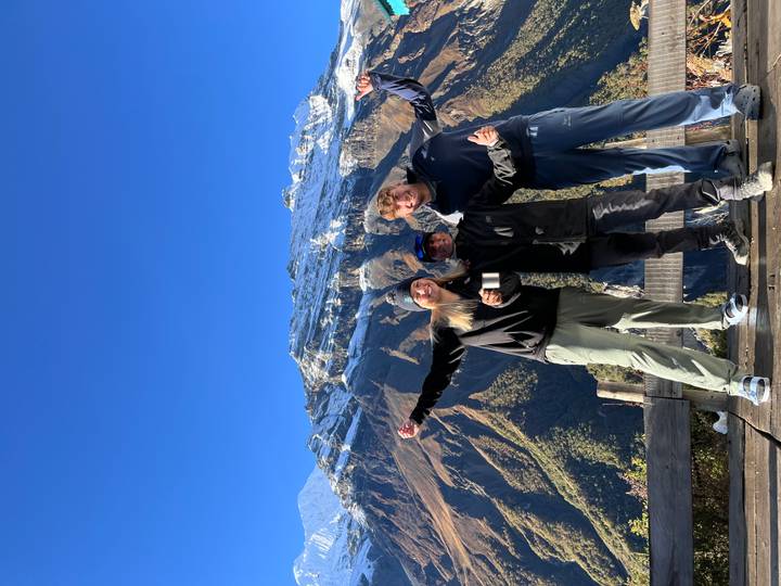 Three people excitedly posing in front of snow-capped mountains.