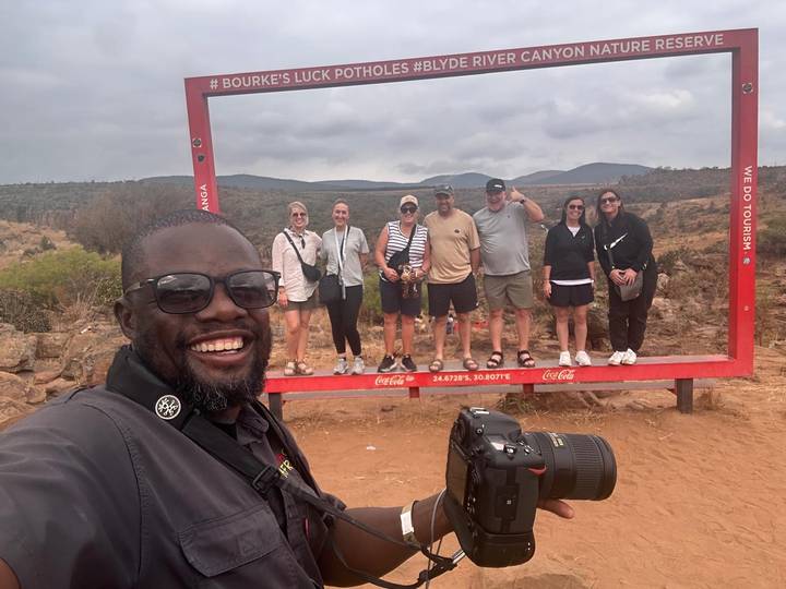 Groupe posant à l'intérieur d'un grand cadre avec un arrière-plan pittoresque.