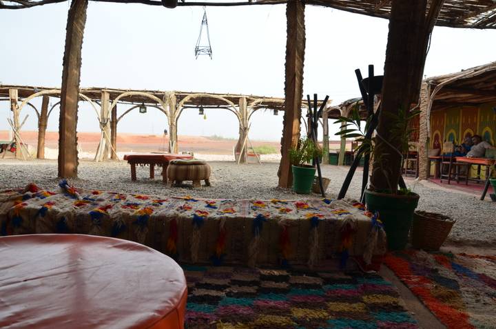 Inside a rustic outdoor gathering area with carpets and cushions.