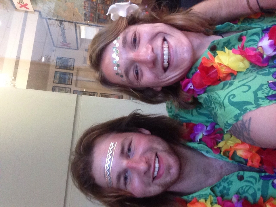 Two people smiling in tropical-themed attire with decorative markings on their faces.
