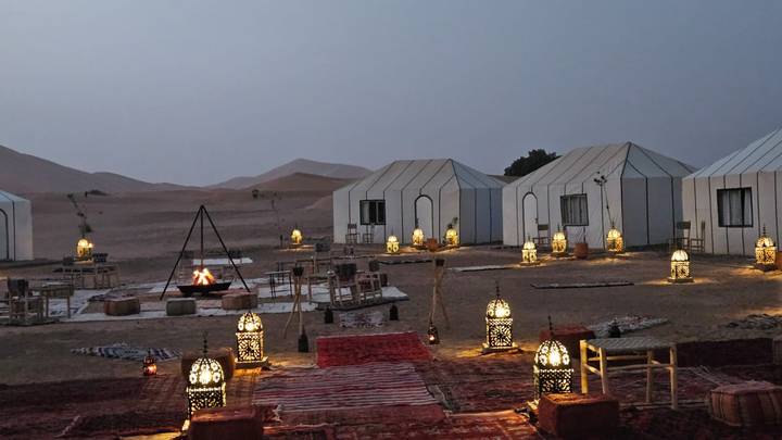 Campement du soir dans le désert avec lanternes allumées et tentes.
