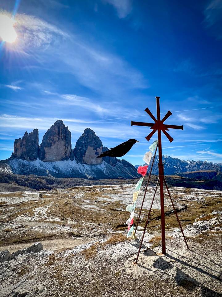 Montagnes avec une croix en métal et un oiseau au premier plan.