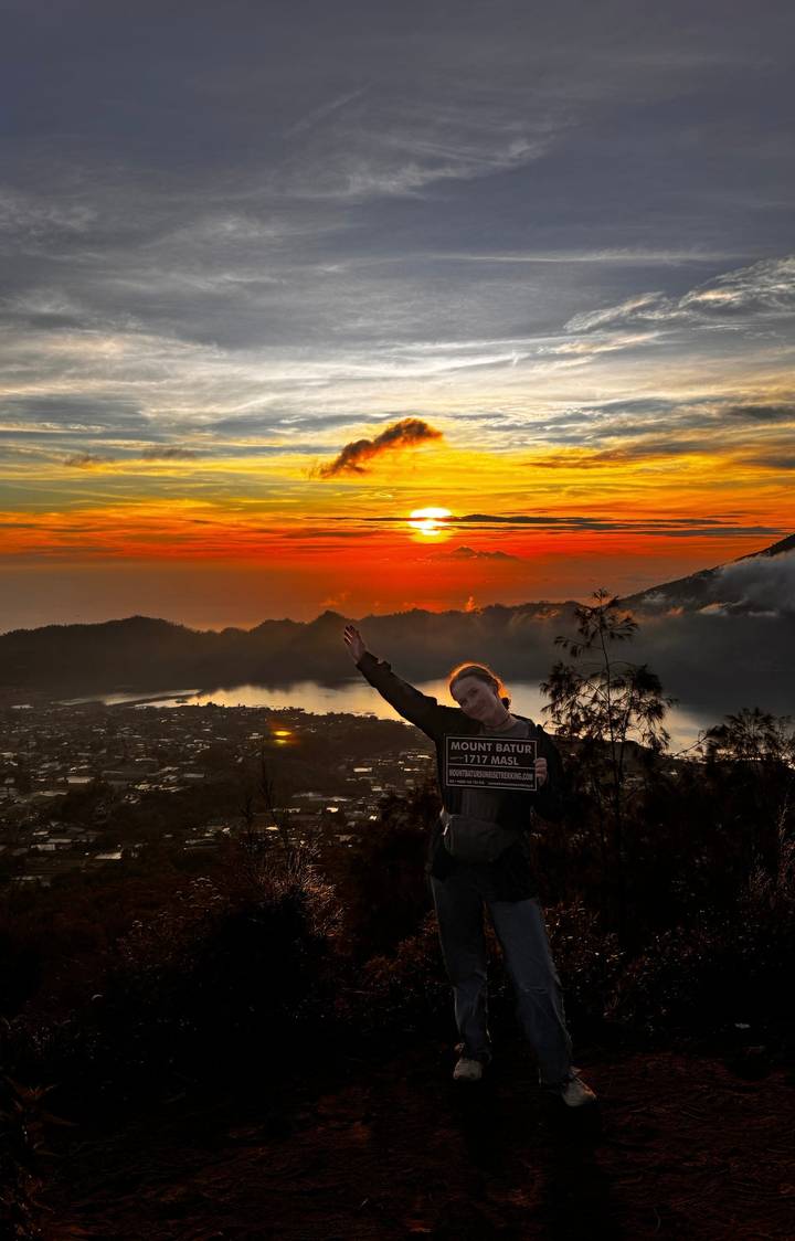 Personne posant avec un panneau devant un coucher de soleil sur le mont Batur.