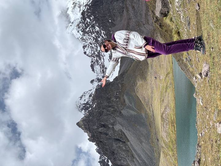 Personne posant avec des montagnes enneigées et un lac.