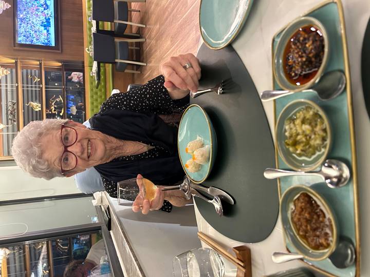Une femme âgée savourant un repas avec un verre de vin.