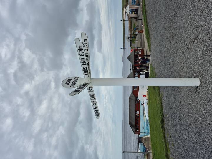 Panneau indicateur de John O'Groats avec indicateurs de distance et visiteurs autour.