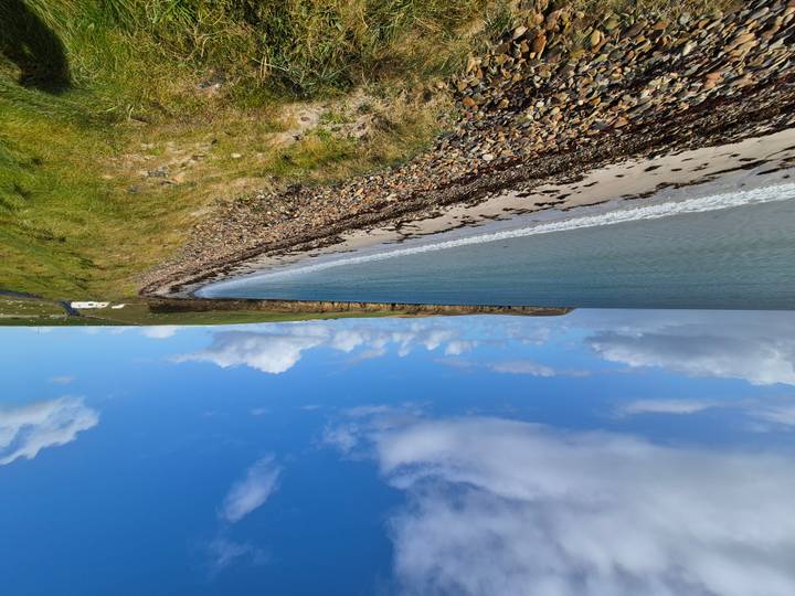 Une vue panoramique d'une plage avec une eau bleue claire et un ciel nuageux.