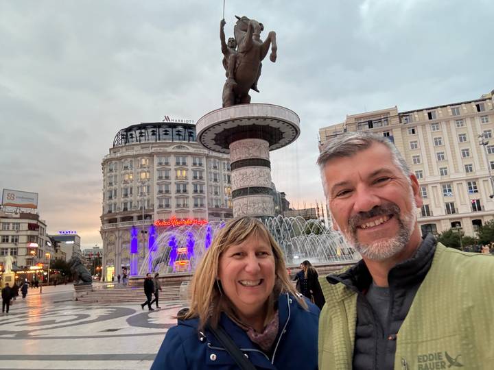 Couple souriant devant une fontaine de ville au lever ou coucher du soleil.