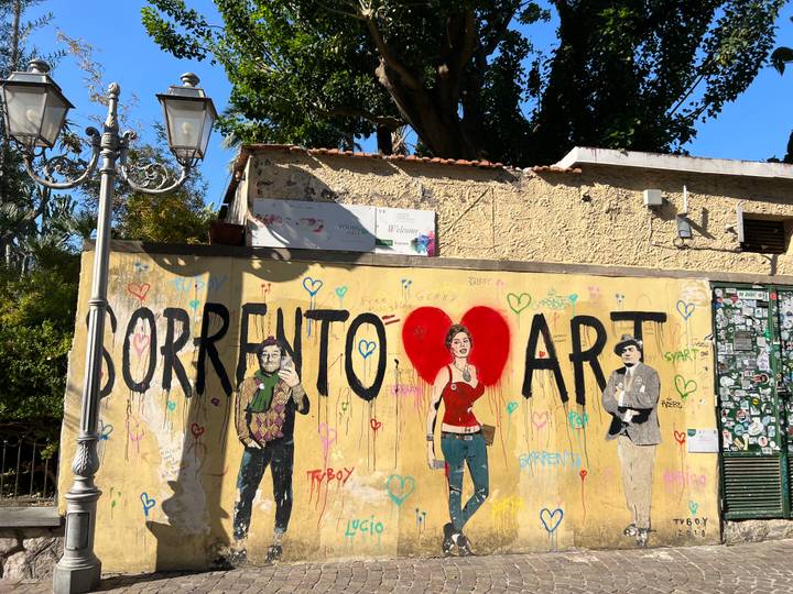 Art mural coloré intitulé 'Sorrento Art' avec des personnages et des cœurs, lampadaires à proximité.