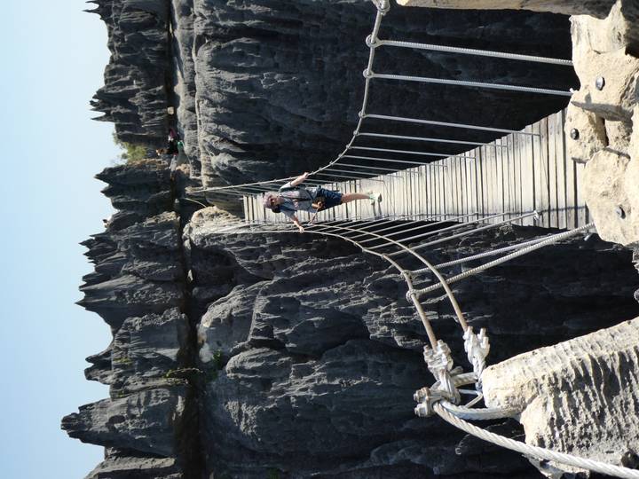 Personne traversant un pont suspendu au-dessus de formations rocheuses déchiquetées.