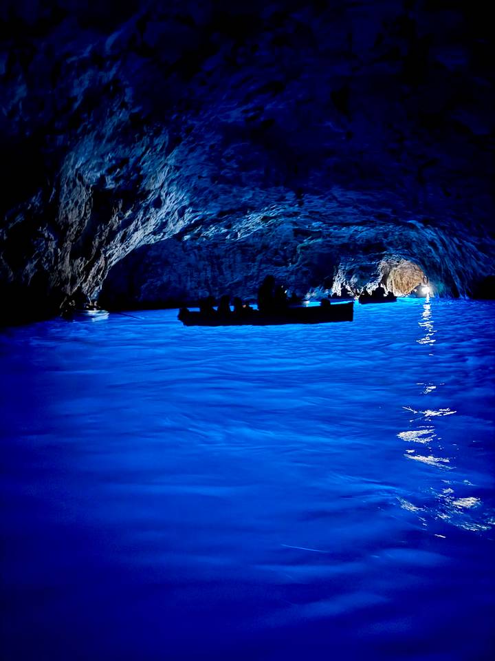 Grotte sombre avec de l'eau bleu électrique et des bateaux.