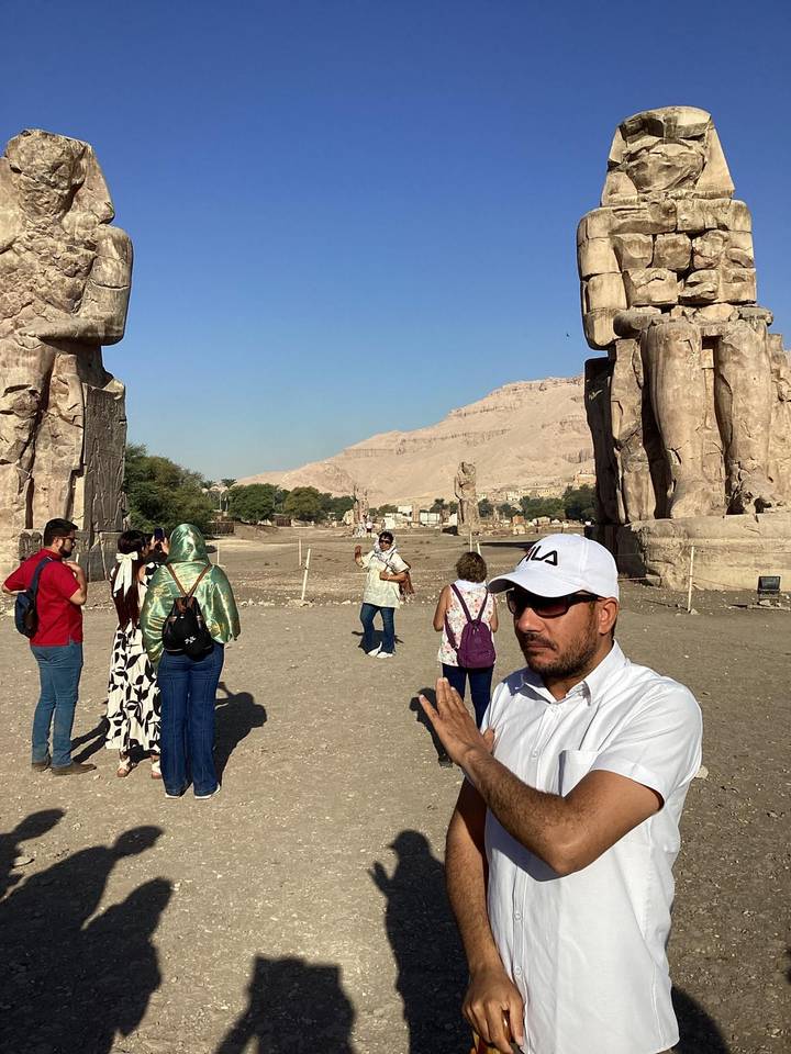 Tourists at ancient ruins with statues in a desert landscape.