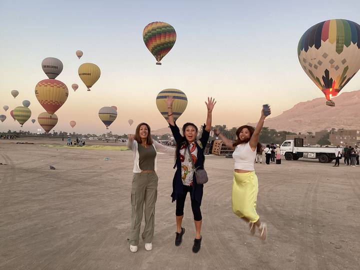 Three people jumping with hot air balloons in the background.