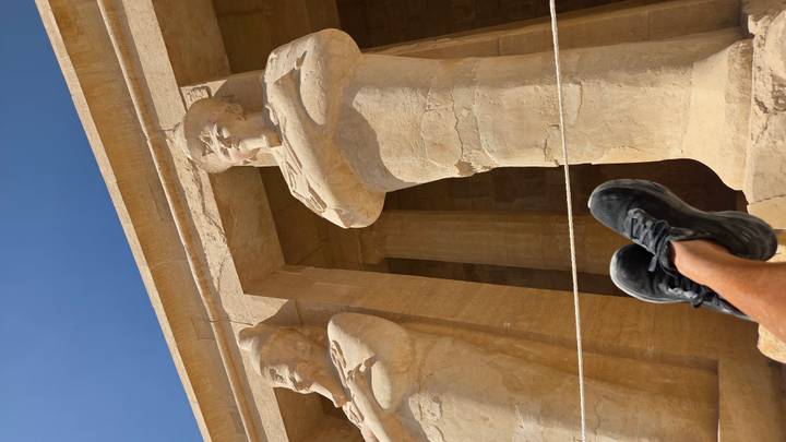 Ancient Egyptian statues with a person's feet visible in the foreground.
