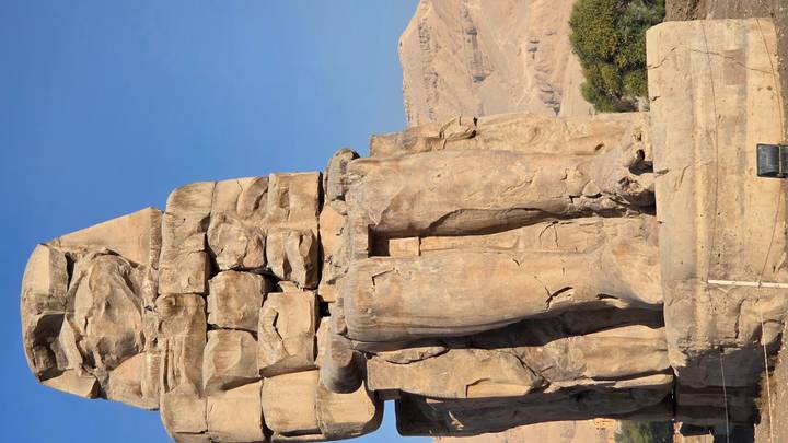Colossal ancient Egyptian statue in a desert setting.