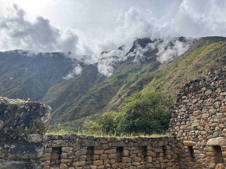 Wolkengeküsste Berge mit alten Steinmauern im Vordergrund.